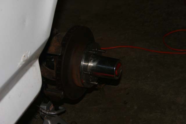 close-up of a vehicle's front wheel hub, brake rotor, and part of the white fender