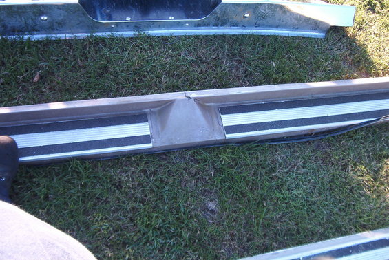 Close-up of a metal step bumper with black and silver non-slip strips. A crack is visible in the center