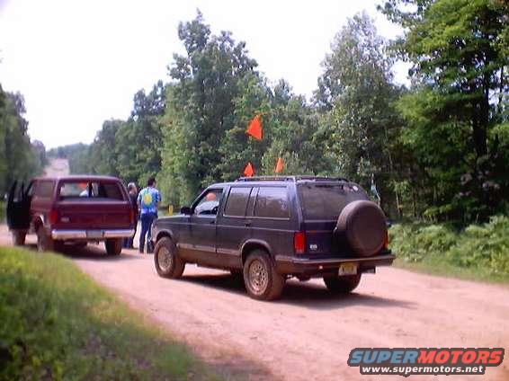 Dark SUV with a spare tire on the rear door, parked on a dirt road