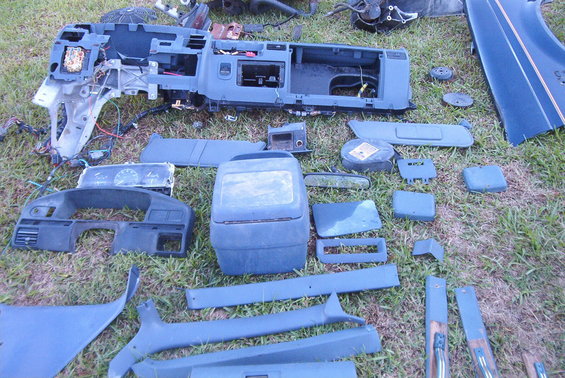 Vehicle interior parts laid out on grass, including dashboard sections, console, and trim pieces