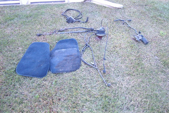 Two blue floor mats and various car parts including a motor and cables laid out on grass