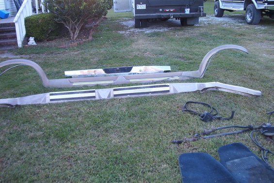 Trim pieces and some car parts laid out on grass. A truck and SUV are in the background