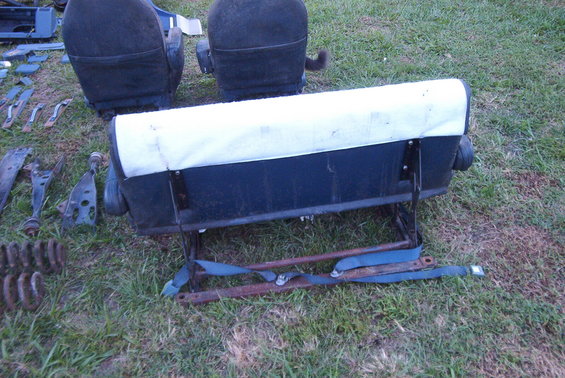 Two dark blue and white vehicle seats and assorted metal parts laid out on grass