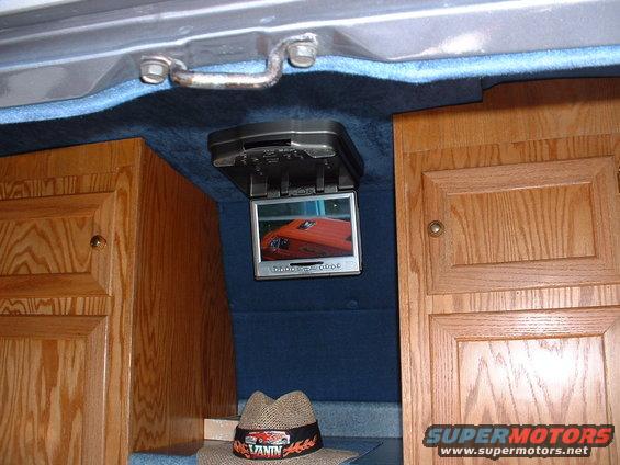 Van interior with wood cabinets and flip-down screen displaying an orange vehicle