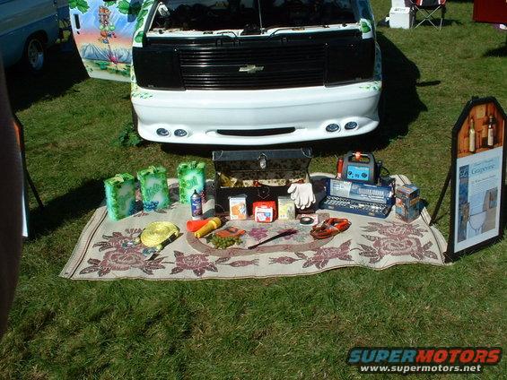 Front view of a white van with a black grille, parked on grass next to a display of tools and items