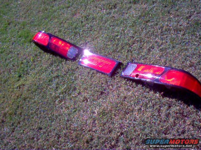 Two red car tail lights, one with 'GT' text, lying on grass