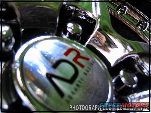 Close-up of a chrome emblem with red 'R' and black '12' text, possibly from a racing part