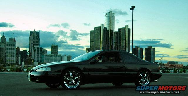 Black coupe with chrome wheels parked in front of a city skyline
