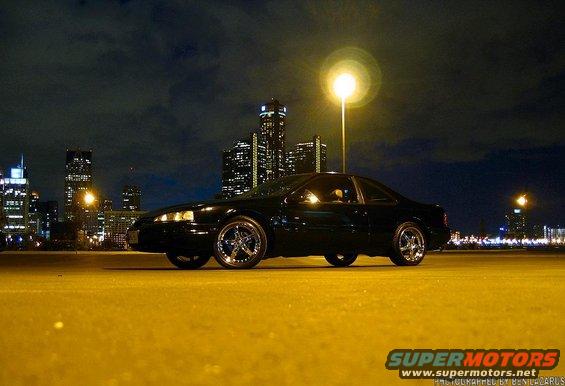 Black coupe parked at night with city lights in the background