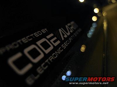 Black car door with "PROTECTED BY CODE ALARM ELECTRONIC SECURITY SYSTEM" sticker and bokeh lights