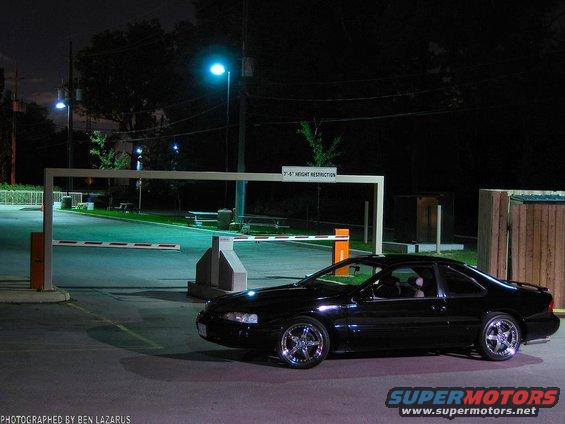 Black coupe with chrome wheels parked at night near a gate