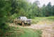 1978 Ford Bronco - 1978 Ford Bronco navigating a wet, off-road path surrounded by trees.