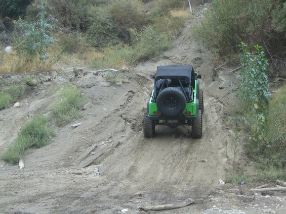 Green 1987 Suzuki Samurai with a spare tire mounted on the rear, driving up a dirt hill