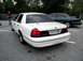 1998 Ford Crown Victoria - A white 1998 Ford Crown Victoria is parked in a lot, with another vehicle visible behind it.