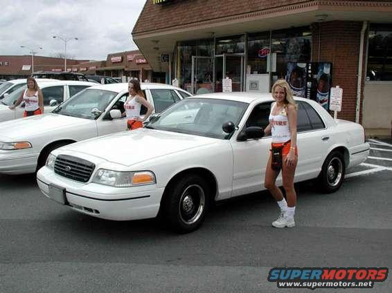 Two white Ford Crown Victorias parked outside a building with women standing next to them