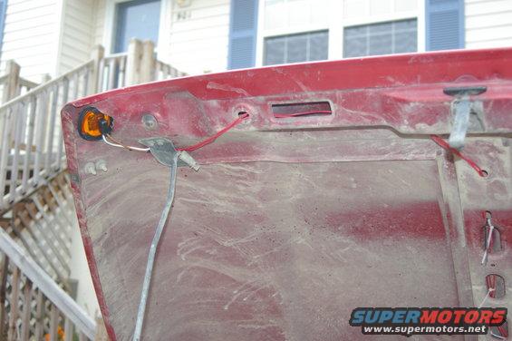 Underside of red car hood showing wiring and amber marker light assembly