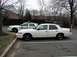 1998 Ford Crown Victoria - Two white police sedans are parked side-by-side, with the closest one showing "ALEXANDRIA POLICE" on its door.