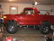 1979 Ford Bronco - Side profile of a red Ford Bronco, modified with a lift kit and custom wheels, inside a garage.