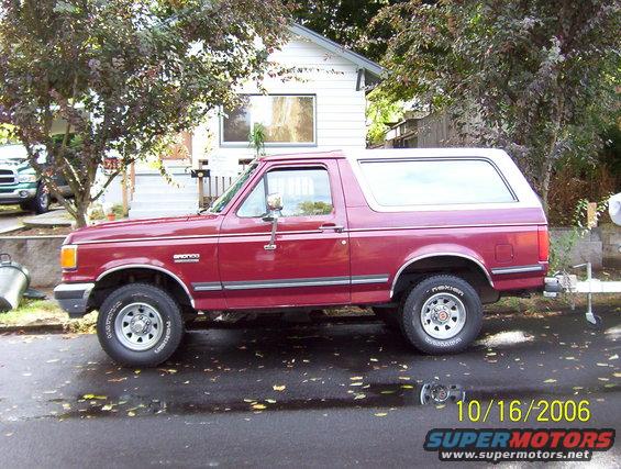 Red 1991 Ford Bronco parked on street, side view. Trailer hitch visible
