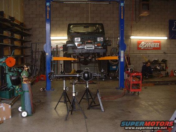 Dark green Jeep Wrangler on a lift with its rear axle removed