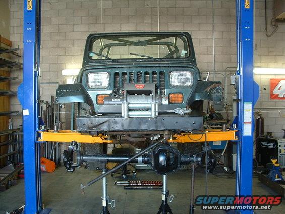 Green Jeep YJ on a lift with front end disassembled, winch mounted