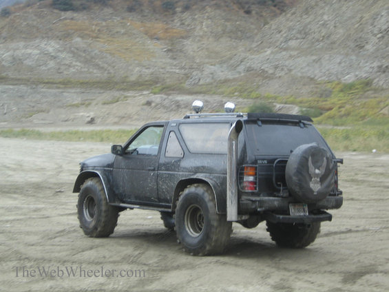 Modified black SUV with large tires and side exhaust pipe parked on dirt