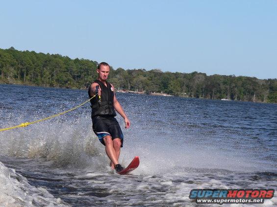 Waterskier on a red ski being pulled by a boat, creating a large spray
