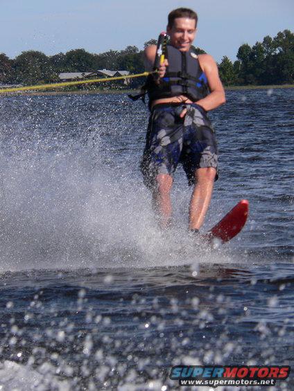 Guy waterskiing, kicking up spray. He's wearing a life vest and board shorts