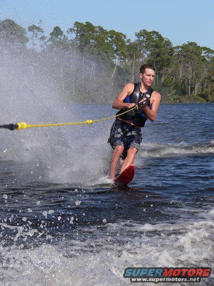 Waterskier on red ski behind boat, spray in air