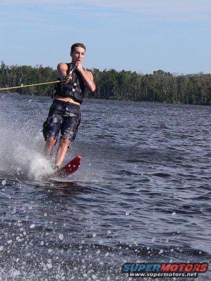Man water skiing on a lake, holding a tow rope, wearing a life vest and shorts