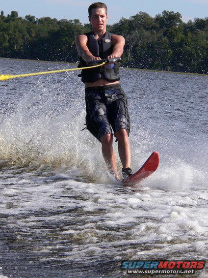 Guy waterskiing, holding tow rope, wake behind him