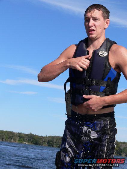 Man in life vest on water, blue sky and trees in background