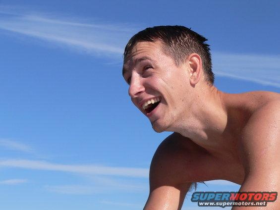 Man laughing with blue sky and clouds behind him. Supermotors.net logo visible