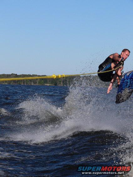 Wakeboarder mid-air over water splash, yellow tow rope visible