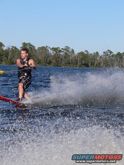 Man water skiing behind a boat, creating a large spray