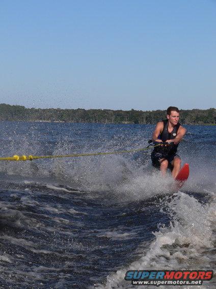 Waterskier on a red ski being pulled by a boat, creating a large spray of water