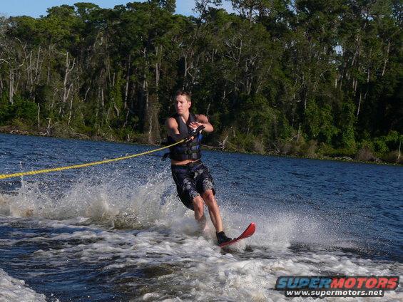 Man waterskiing on a lake with trees in the background. Water sports