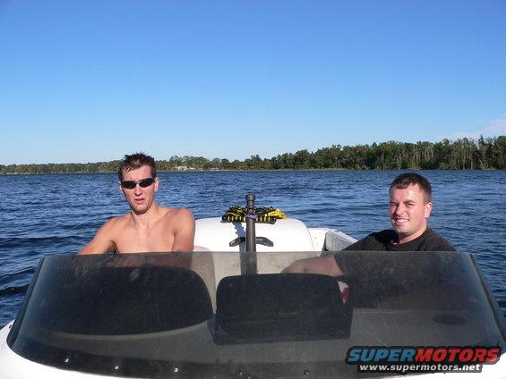 Two men in a white boat on a blue lake under a clear sky