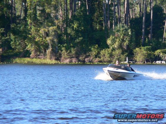 Boat speeding on a lake with trees in the background. Two people are onboard