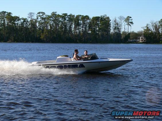 White speed boat with blue lettering 'MOOMBA' on its side, cutting through blue water with a wake