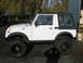 1987 Suzuki Samurai - This Suzuki Samurai is parked on a gravel surface with a building and trees visible behind it.