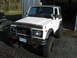 1987 Suzuki Samurai - A white 1987 Suzuki Samurai is parked in a garage, modified for off-road use with a bull bar and large tires.