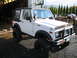 1987 Suzuki Samurai - This lifted 1987 Suzuki Samurai features oversized tires and a black soft top, parked in a garage setting.