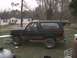 1988 Ford Bronco - A black Ford Bronco with a red stripe is parked in a grassy yard next to a house.