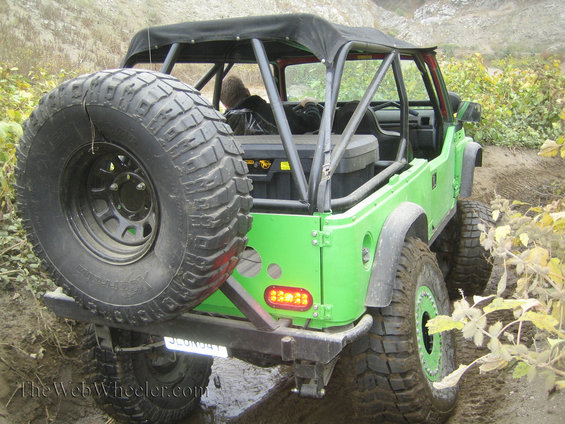 Green off-road SUV with large spare tire on back, driving on a dirt trail