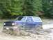 1989 Ford Bronco - A blue Ford Bronco navigates a muddy terrain, kicking up dirt and water.
