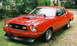 1975 Ford Mustang II - Red 1975 Ford Mustang II coupe with a black hood scoop and side stripe parked outdoors.