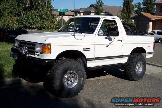 White 1989 Ford Bronco lifted with oversized tires, parked on a street