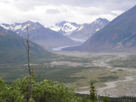 Mountain valley with a winding glacier and river under a cloudy sky