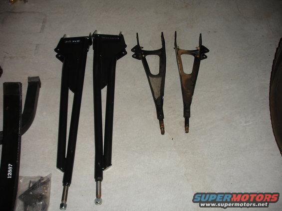 Two black suspension control arms and two rusty control arms on a concrete floor